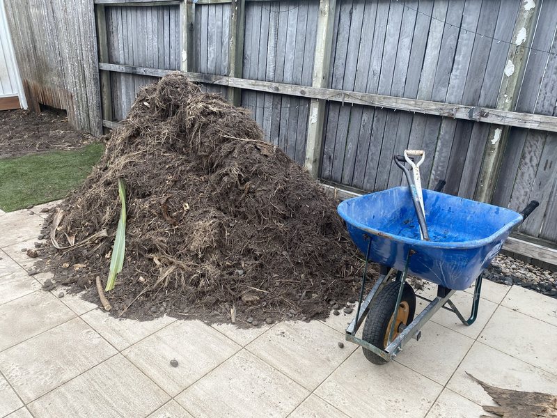 A large garden waste pile against a fence before removal